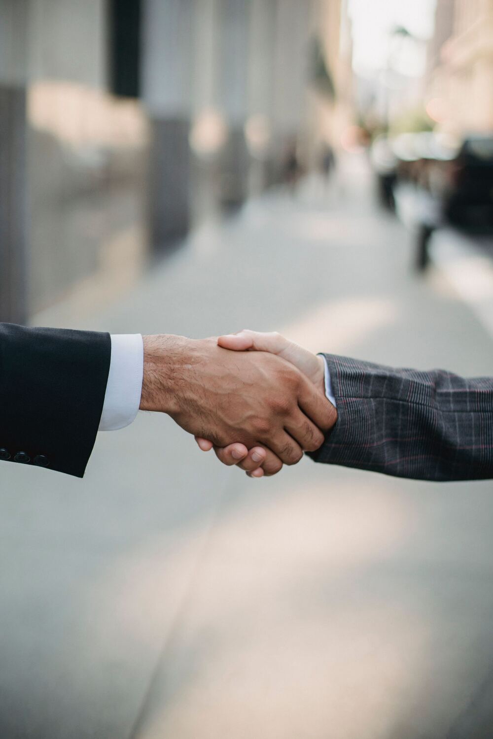 Two people shaking hands on a sunlit sidewalk after reaching an agreement